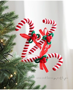 Three red and white candy cane ornaments with green holly bows on a lit Christmas tree