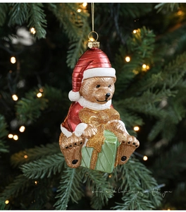 Detail of teddy bear Christmas ornament with red coat and gift box hanging on a tree