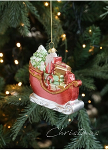 Detail of red Christmas sleigh ornament with miniature tree and gifts on pine branch