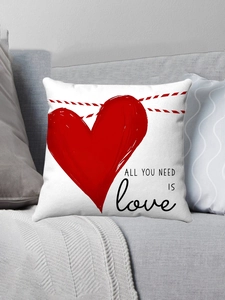Dettaglio cuscino in peluche bianco con cuore rosso e testo All You Need Is Love su divano