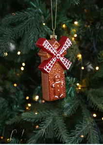 Close-up of a gingerbread house windmill ornament hanging on a Christmas tree with warm bokeh