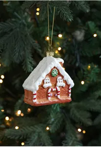 Close-up of a gingerbread house Christmas ornament with faux snow on a green pine tree