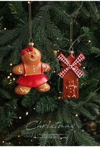 Close-up of gingerbread girl and cottage ornaments hanging on a lighted Christmas tree