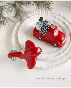 Detalle de adornos navideños de camión rojo y avión con cordones dorados finos