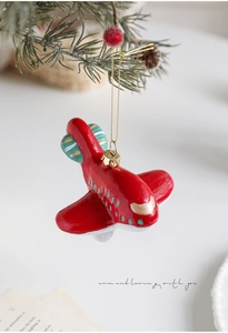 Detalle de adorno de avión rojo colgado en una rama de pino con decoración navideña