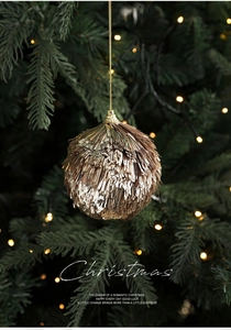 Detail of a sparkling gold sequin Christmas ball hanging on a green tree with warm lights