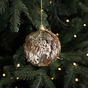 Champagne gold glitter fringe Christmas ball ornament hanging on a festive pine tree