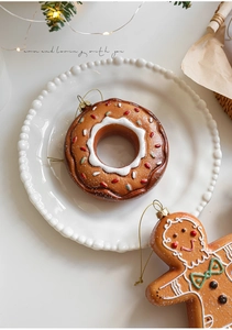 Festive gingerbread man and donut Christmas ornaments on a decorative white plate