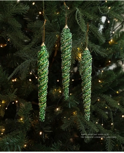 Close-up of green glitter icicle ornaments with gold beads on a lighted Christmas tree