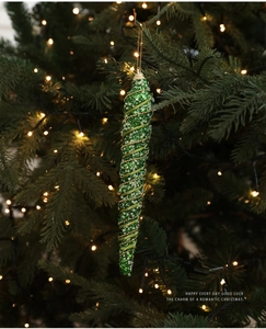 Detail of green spiral Christmas icicle ornament with golden beads on a lit tree