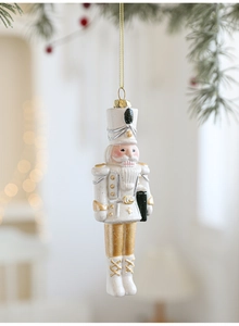 Détail d'une suspension Casse-Noisette blanc crème et or accrochée à une branche de pin