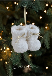 Detail van witte pluche kerstlaarzen met gouden strikken aan een versierde kerstboom
