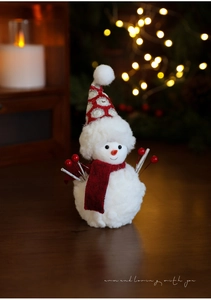 Close-up of plush snowman doll with red scarf and berries on warm wooden desk