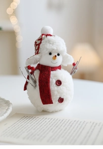 Close-up of a plush Christmas snowman doll with a red scarf on a cozy lit desk