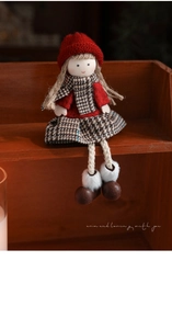 Detail of plush Christmas doll in red knit hat and plaid skirt on a wooden shelf