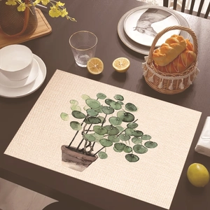 Detail of a tropical Pilea plant print placemat on a dark wooden dining table