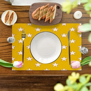 Detail of yellow star placemat on wood table with dinnerware and floral decor