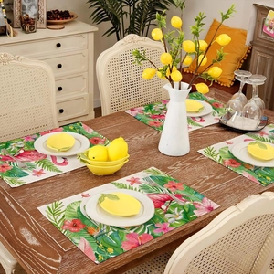 Set of four tropical placemats with pink flamingo and green palm leaves on dark wood table