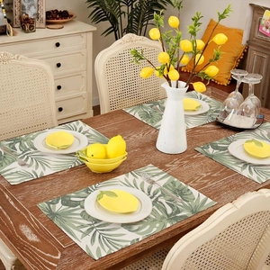 Detail of four tropical green leaf placemats on a rustic wooden dining table setup