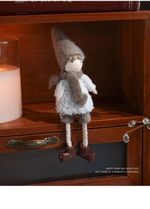 Detail einer Plüsch-Weihnachtspuppe im weißen Pullover auf einem Holzschrank sitzend