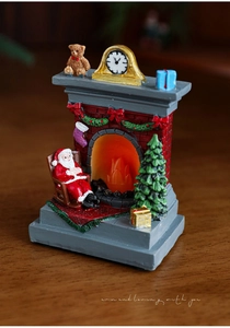 Close-up of a lit resin Christmas fireplace ornament with a miniature Santa and tree