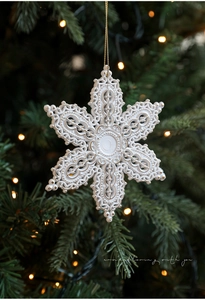Detailed view of a white and gold snowflake ornament hanging on a festive Christmas tree