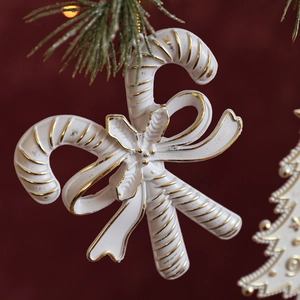 Matte white candy cane Christmas ornament with gold trim on green pine branch