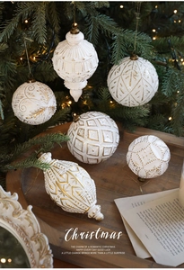 Nahaufnahme von weiß-goldenen Weihnachtskugeln mit handgemalten Mustern am Baum