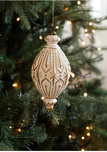 Detail eines weißen Weihnachtsanhängers mit goldener Prägung am beleuchteten Baum
