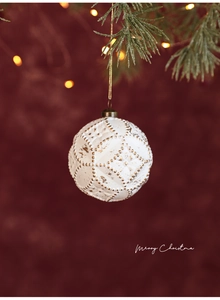 Nahaufnahme einer weiß-goldenen Weihnachtskugel mit geometrischem Muster an einem Kiefernzweig
