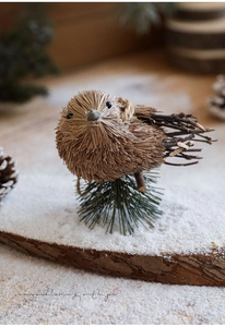 Handgefertigte Stroh-Vogelfigur mit verschneiten Zweigen auf einem Holzsockel