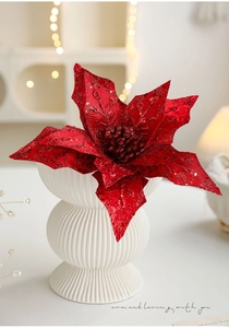 Close-up of artificial red poinsettia with glitter petals in a stylish white ceramic vase