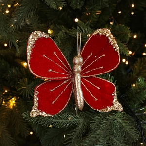Red velvet Christmas butterfly ornament with gold glitter and pearls on a tree branch