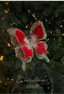 Détail d'un papillon de Noël en velours rouge avec paillettes dorées sur un sapin vert