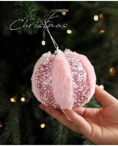 Pink plush Christmas ball with faux fur and pearls hanging on a green tree
