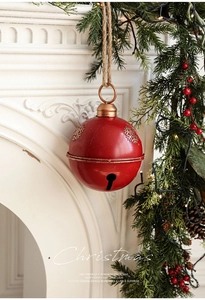 Red metal Christmas bell ornament with gold snowflakes hanging by a fireplace