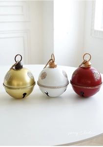 Detailed view of red, white, and gold Christmas bells with snowflake embossing and jute rope