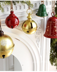 Festive red, green and gold metal Christmas bells with snowflake patterns hanging by jute rope