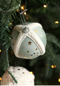 Close-up of green fabric Christmas ball with gold stars hanging on pine tree branches
