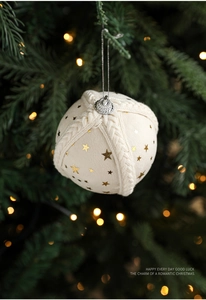 Close-up of 8cm cream fabric Christmas ball ornament with gold stars on a pine tree