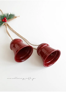 Close-up of red metal Christmas bells with pine needles and berries on white backdrop