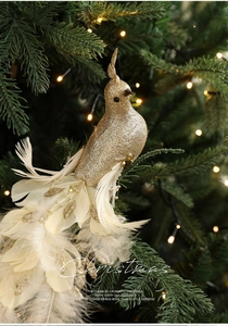 Sparkling gold foam bird ornament with white feathers hanging on a lit Christmas tree