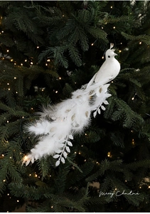 Close-up of white peacock Christmas ornament with faux feathers on green branches