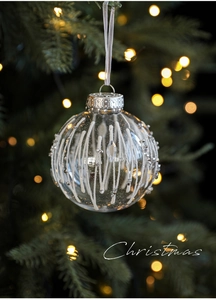 Detailed view of clear Christmas ball with white stripes and silver beads on a tree