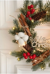 Close-up of Christmas wreath with LED lights, red berries, pine cones and cotton balls