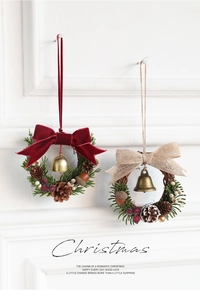 Close-up of two mini Christmas wreaths with pine cones, berries, and bows on a white wall