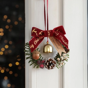 Christmas pine wreath with red velvet bow pinecones and golden bells on white door