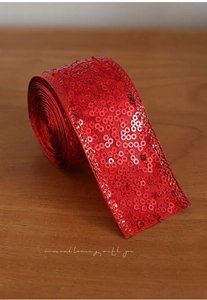 Detail of red sequined ribbon roll on wooden background for Christmas gift wrapping