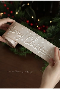 Close-up of champagne Christmas ribbon with Merry Christmas glitter text and snowflake detail