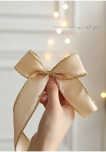 Handheld champagne gold satin Christmas bow with gold trim and warm marketing text